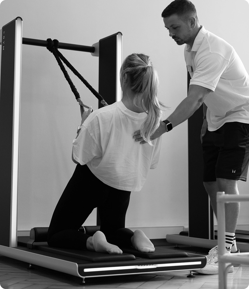 Schwarz Weiß Bild eines Fitnesstrainers der einem Fitnessstudio Mitglied eine Übung zeigt.