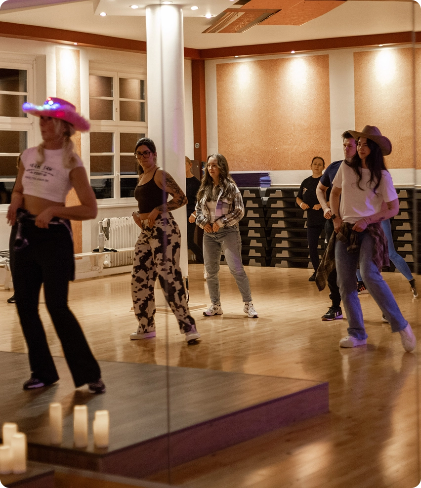 Linedance-Trainerin zeigt im Vordergrund einigen Kursteilnehmern Tanzbewegungen.